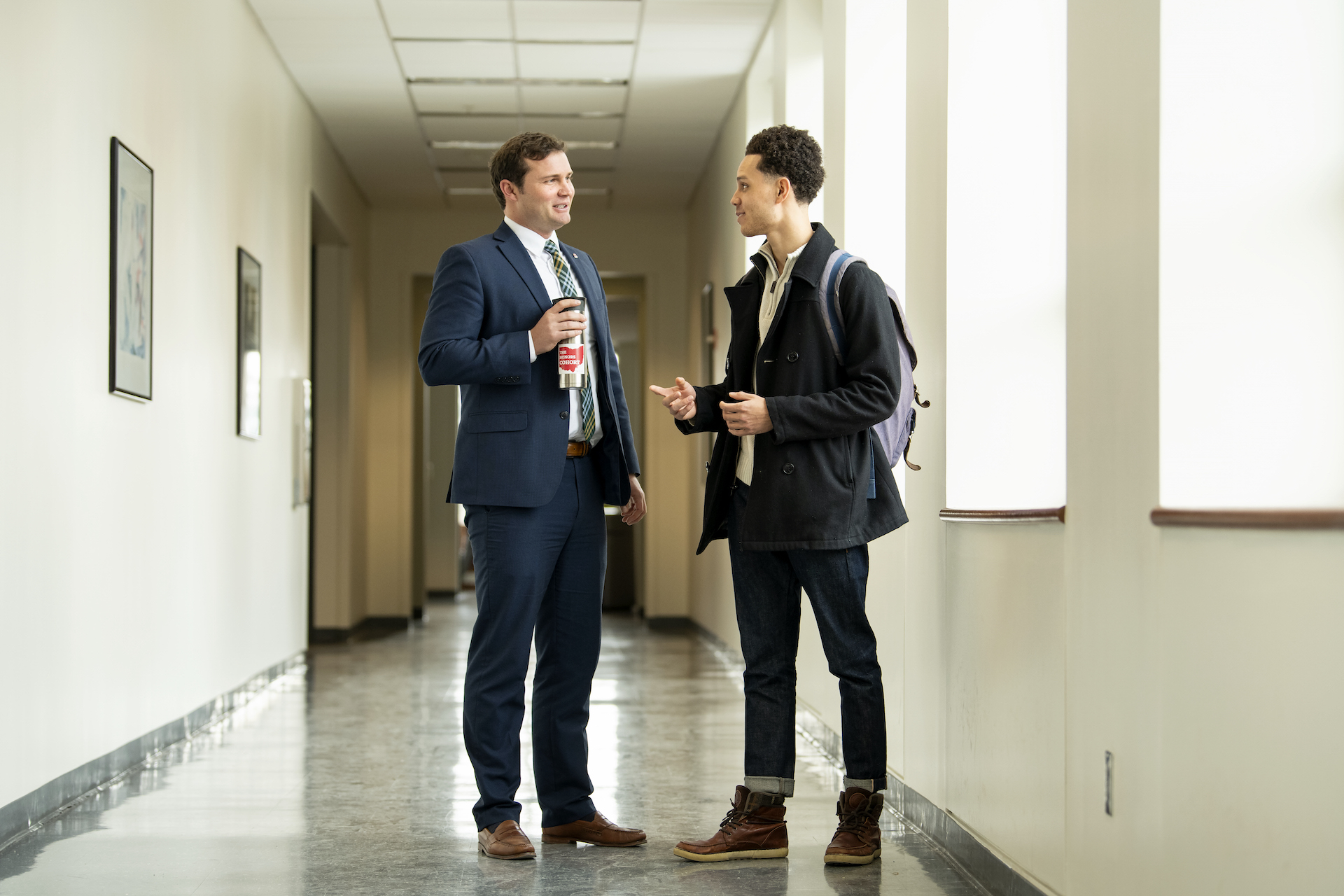 A faculty member speaks with a student in the hallway after class.