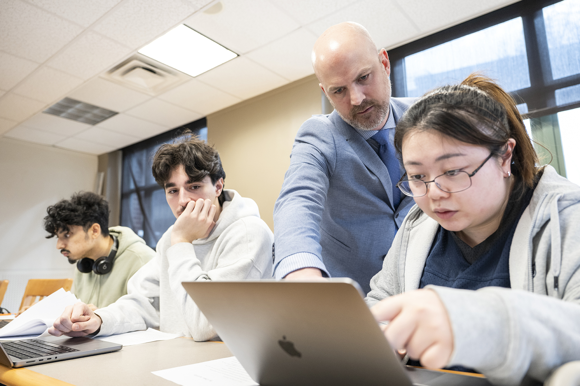 Professor Wallace points to a laptop to help a student, 2 additional students are seated nearby