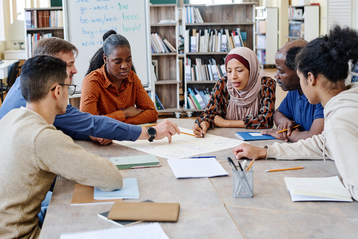 A group of diverse faculty converse around a table covered in documents.