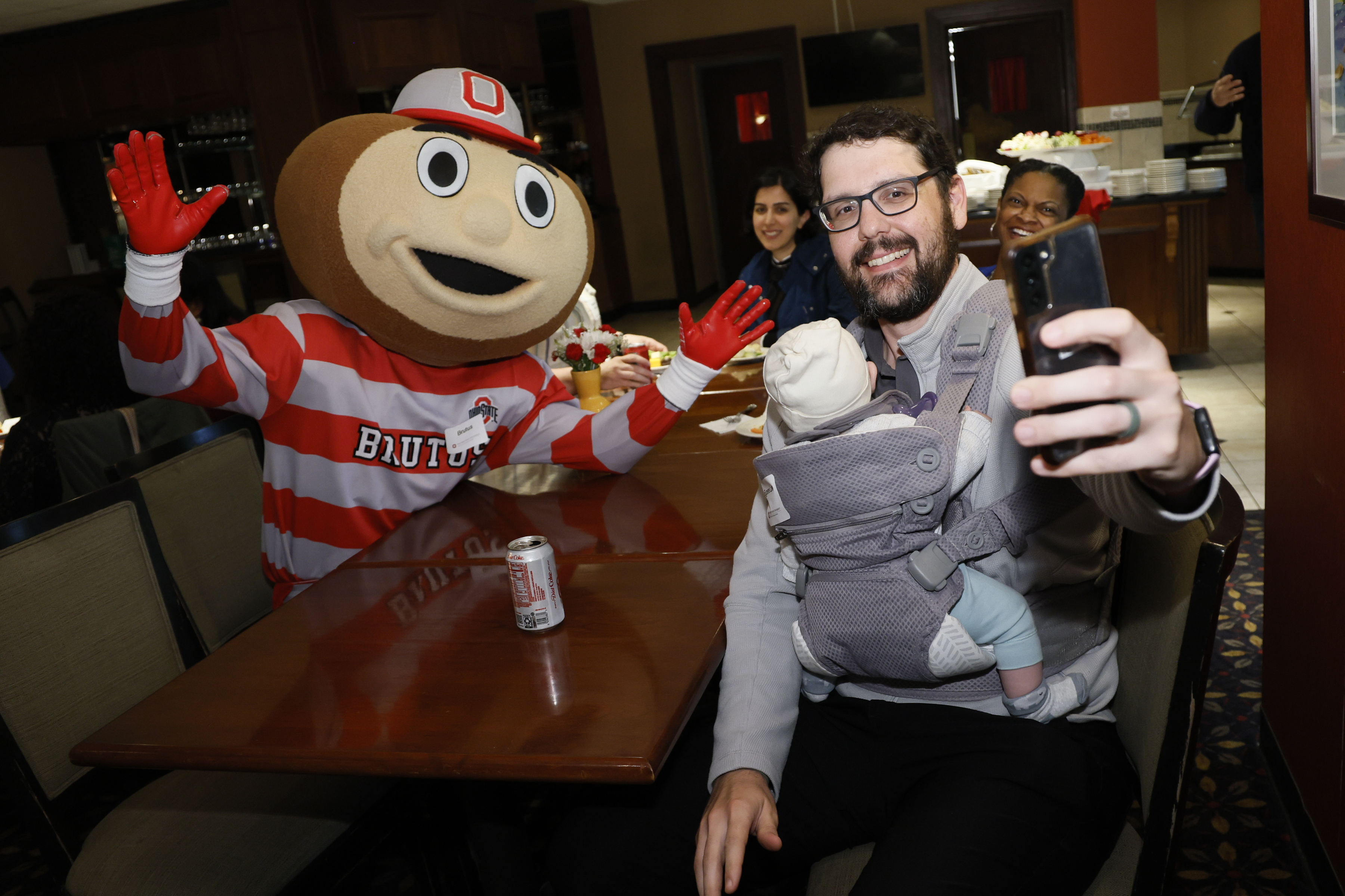 People around a table pose for a selfie with Brutus Buckeye