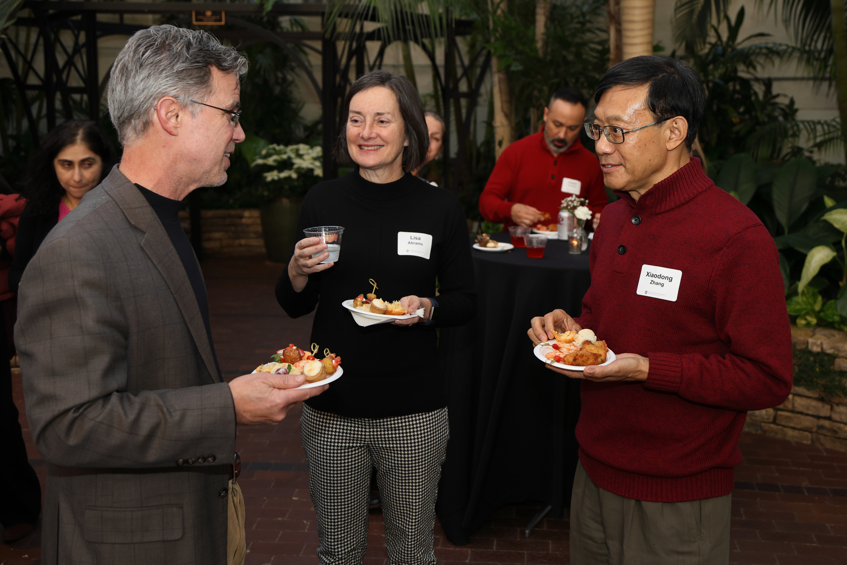 Three faculty members share a conversation in circle with hors d'oeuvres in hand