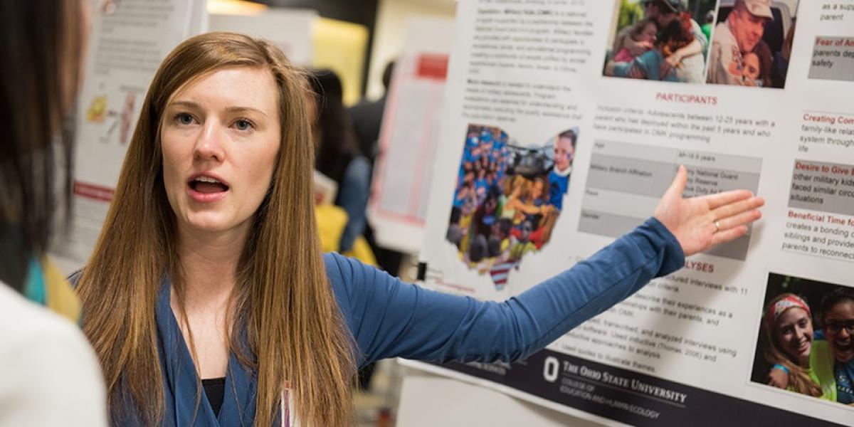 A grad student stands and explains her poster board research.