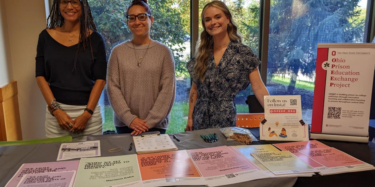 Three woman with pamphlets on a table.