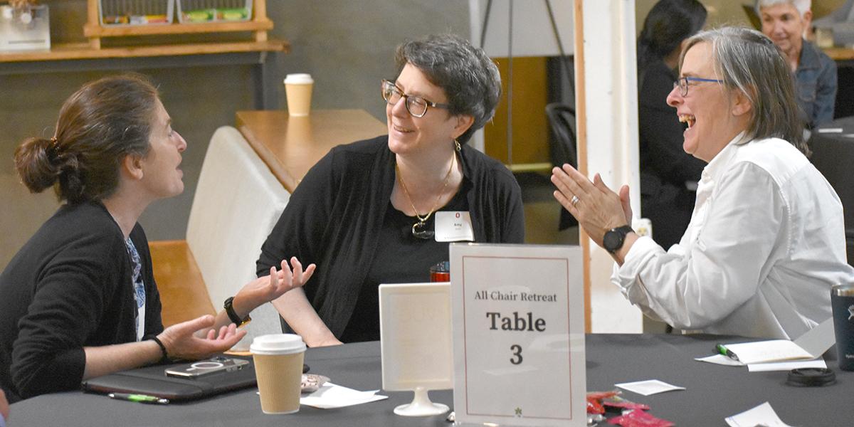 Three individuals share a laugh while conversing at a table