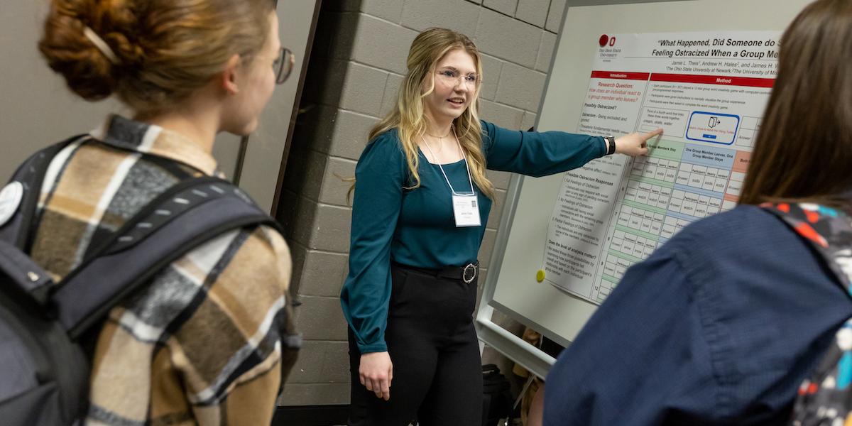 Female student explains poster research to two female students.