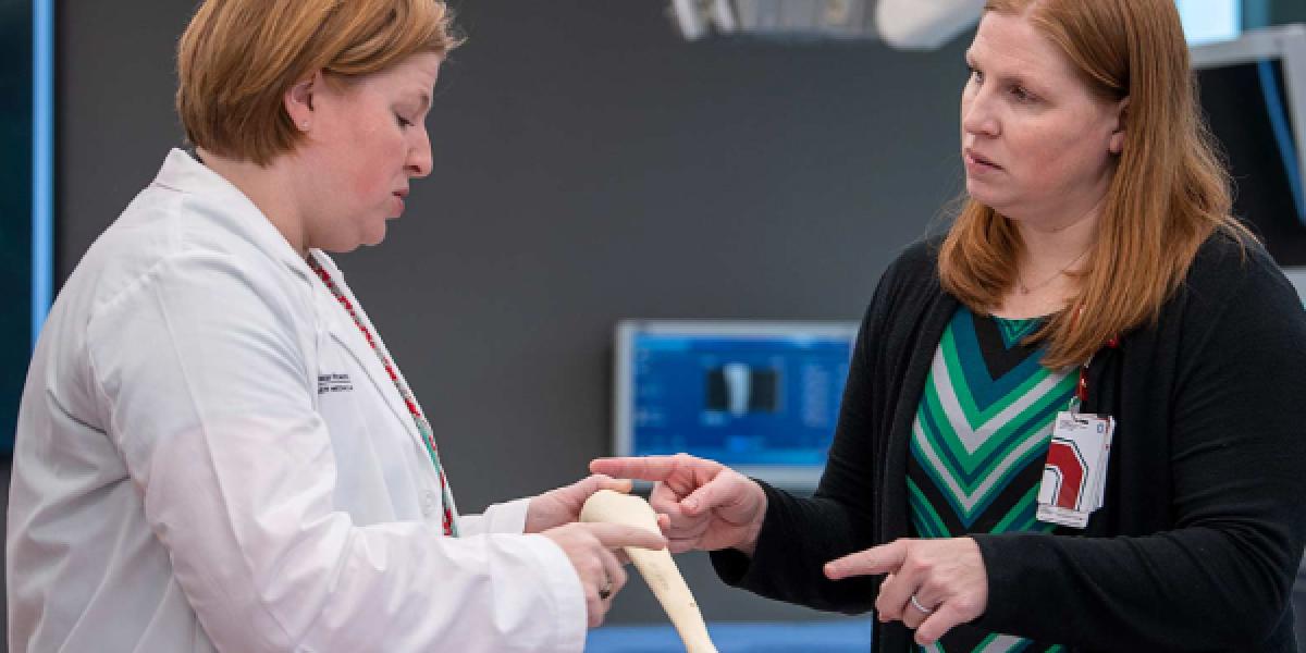 A picture of the Quatman sisters in a medical lab. They are engaged in deep conversation while examining a long, medium sized bone