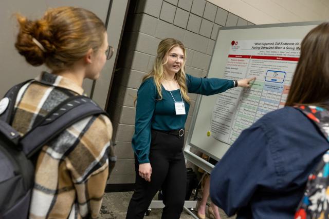 Female student explains poster research to two female students.
