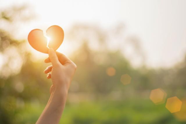 A picture of a hand holding a broken heart up to the sun so that the light shines through.
