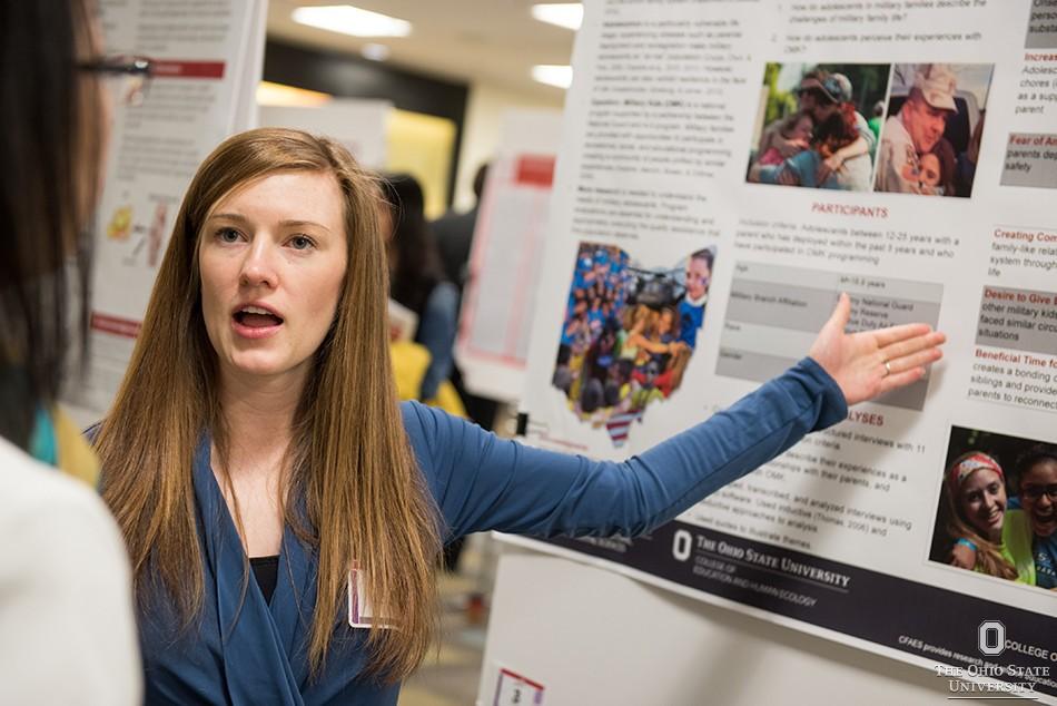 A grad student stands and explains her poster board research.