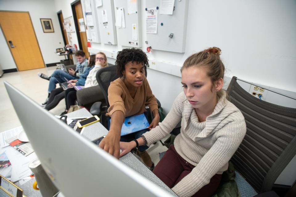 A young black woman professor assists a student on a computer.